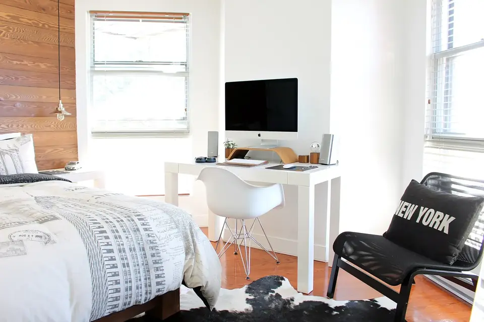 Chambre meublée lumineuse avec un lit, un bureau et une chaise devant une grande fenêtre