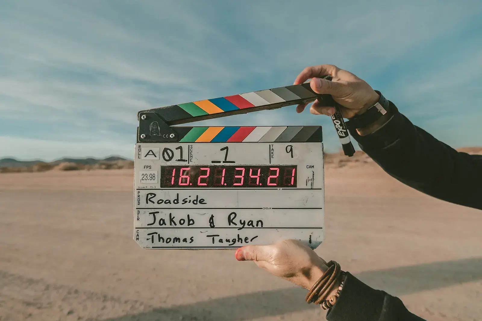 Deux mains tiennent un clap de cinéma ouvert devant un paysage de désert sous un ciel bleu