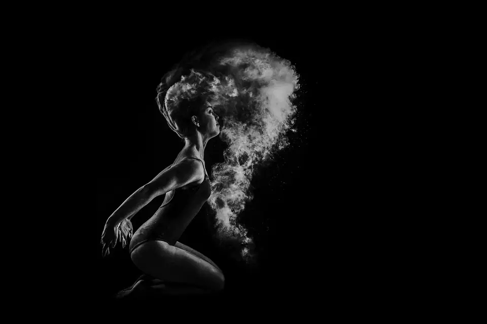 Danseuse en noir et blanc, agenouillée, dans un nuage de poudre claire sur fond noir