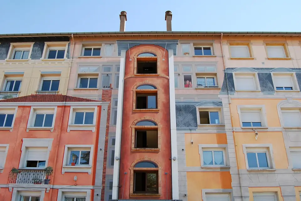Façade d'immeuble ancien aux volets ouverts, peinte de couleurs chaudes, sous un ciel bleu