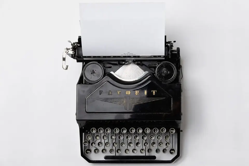 Machine à écrire noire vue du dessus sur un fond blanc, une feuille blanche engagée
