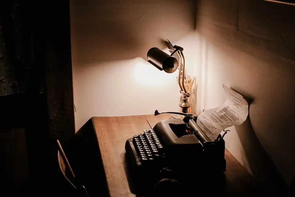 Machine à écrire ancienne sur un bureau en bois, éclairée par une lampe, une feuille engagée dans le rouleau