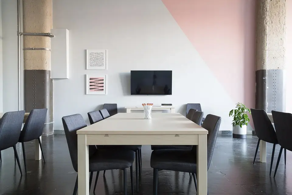 Salle de réunion claire avec une grande table blanche entourée de chaises grises