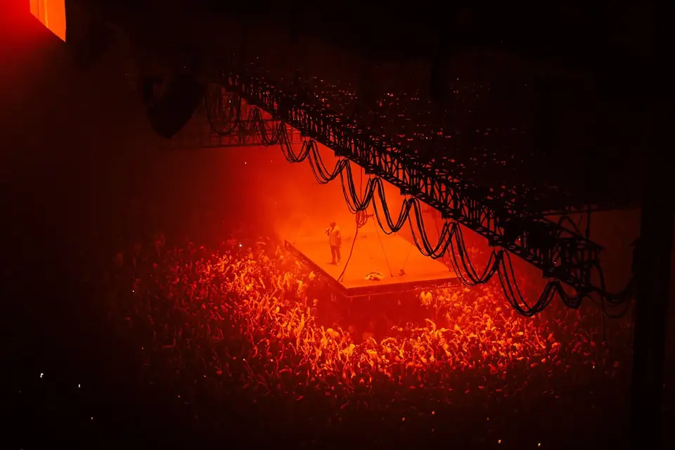 Salle de concert baignée de lumière rouge, vue depuis les hauteurs, avec une structure scénique suspendue