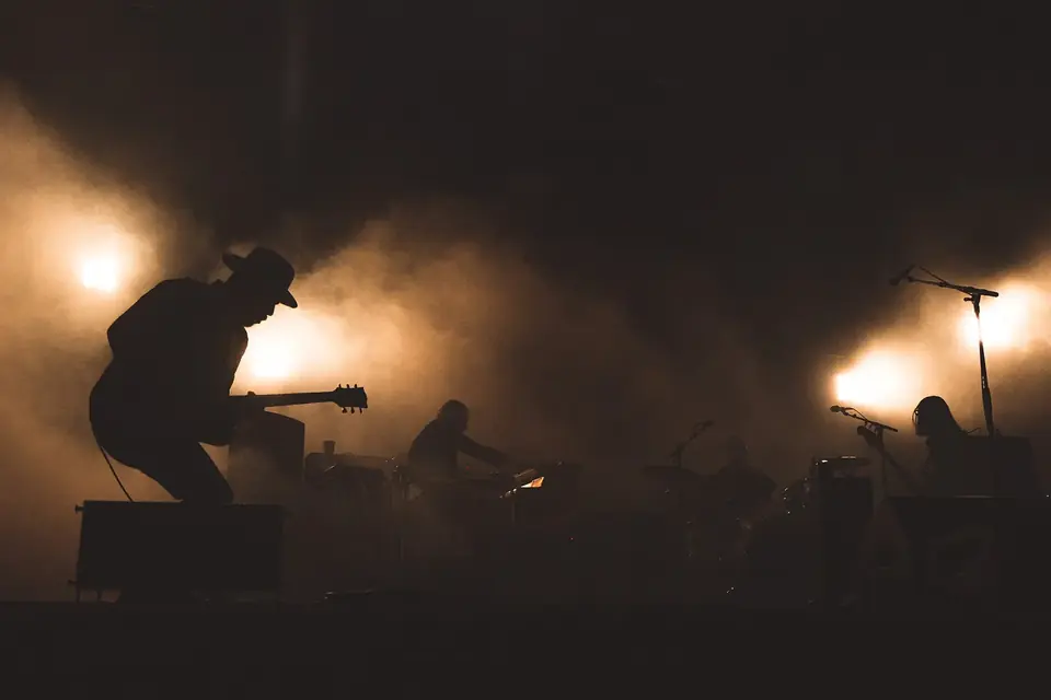 Silhouettes de musiciens sur une scène plongée dans la pénombre, éclairée par quelques projecteurs dans la fumée